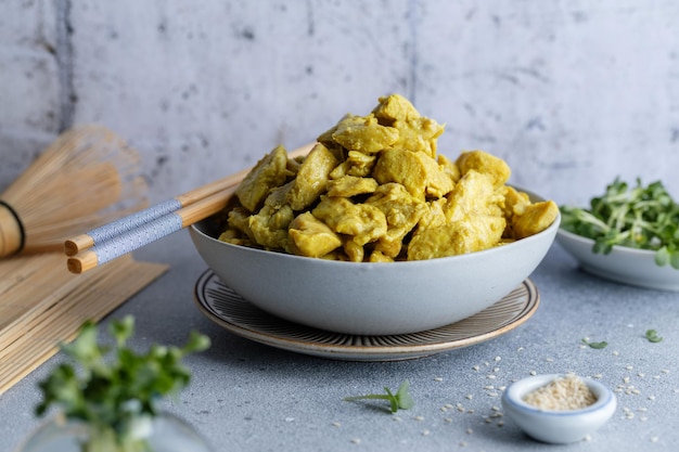 Foto pollo in salsa al curry servito in una ciotola con bastoncini sul tavolo primo piano