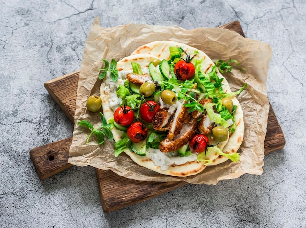 Chicken schnitzel greek gyros with lettuce tzatziki sauce roasted tomatoes cucumbers olives on a cutting board on a light background top view