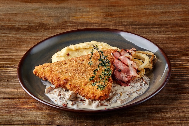 Cotoletta di pollo con purè di patate alle erbe e salsa di funghi su piatto su sfondo di tavolo in legno ...