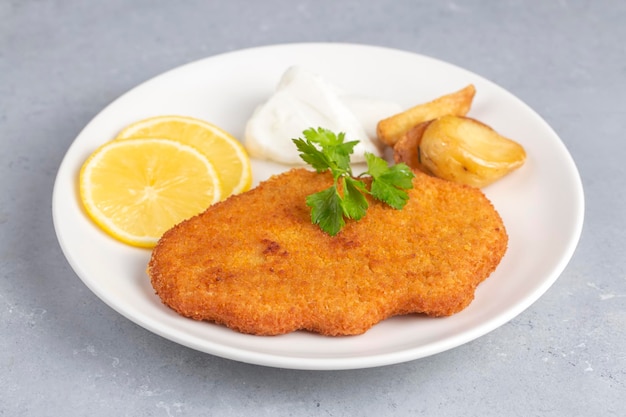 Chicken schnitzel with sauce fried potatoes and lemon in a plate