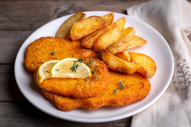 Chicken schnitzel with sauce fried potatoes and lemon in a plate