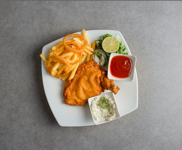Chicken schnitzel with tomato sauce fries lime and salad served in dish isolated on grey background top view of arabic food