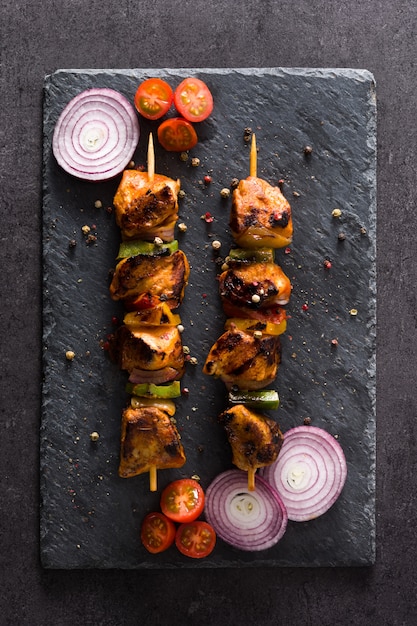 chicken shish kebab with vegetables on black slate top view