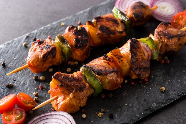 Chicken shish kebab with vegetables on black stone close up