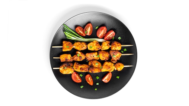 Chicken skewers with vegetables on black plate isolated on white. Souvlaki isolated.