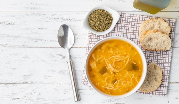 Chicken soup in a bowl with bread slices and seasoning over wooden table with copy space