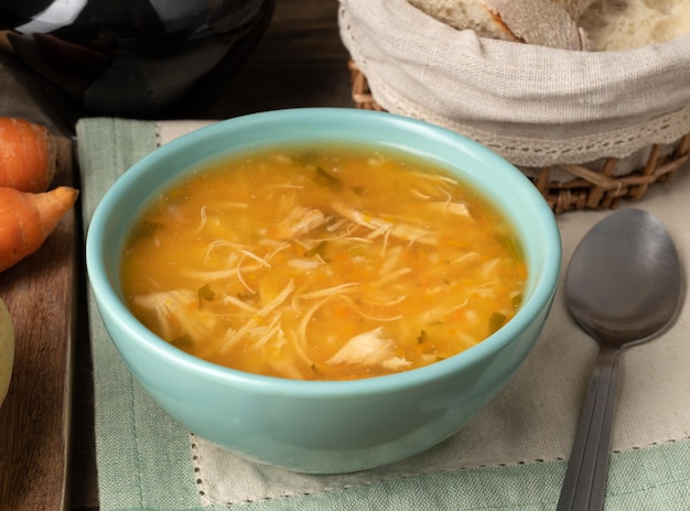 Chicken soup in a bowl with bread slices and wine over wooden table