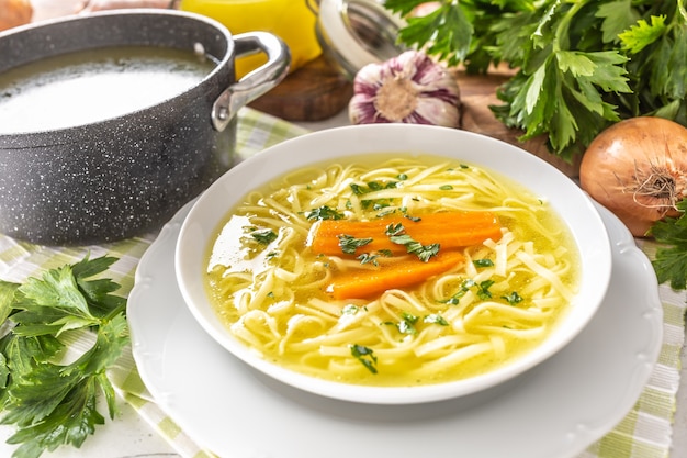 Chicken soup broth in a plate carrot onion celery herbs garlic and fresh vegetables.