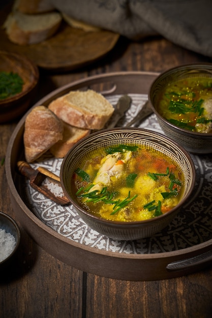 Chicken soup in clay bowls, bread on rustic background.