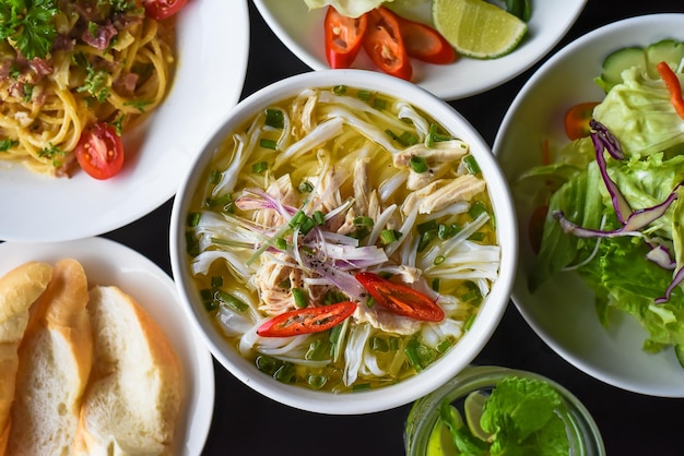 Chicken soup Pho ga  in vietnamese style on black background with banh mi bread, salad and pasta car