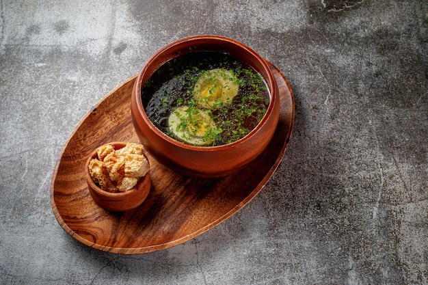 Chicken soup with boiled egg sprinkled with dill and parsley greens in a wooden bowl with bread crumbs stands isolated on a stone table, Flatlay