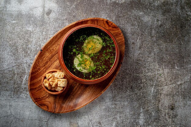 Zuppa di pollo con uovo sodo cosparso di aneto e prezzemolo in una ciotola di legno con briciole di pane si erge isolato su un tavolo di pietra, flatlay