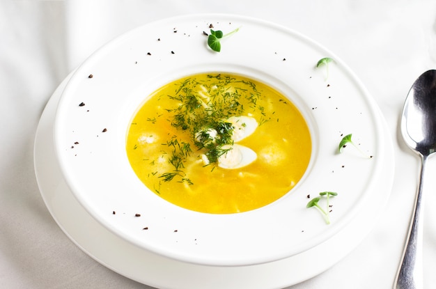 Chicken soup with meatballs and quail eggs on white table