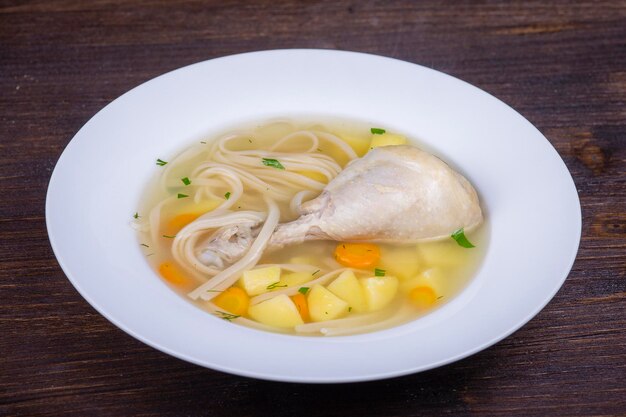 Chicken soup with noodle and vegetables in white plate close up
