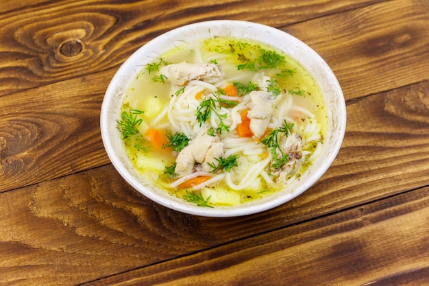 Photo chicken soup with noodles and vegetables on wooden table