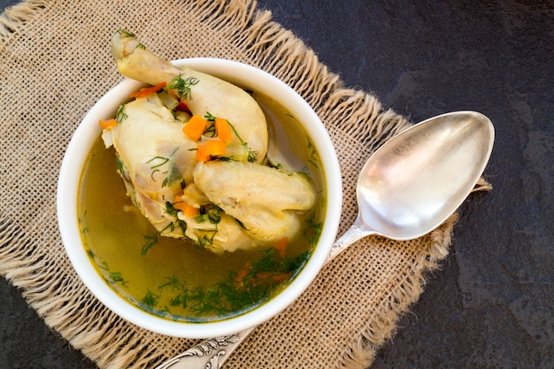 Chicken soup with vegetables on black table.