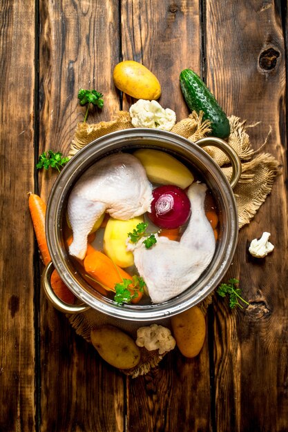 Куриный суп с овощами в большой кастрюле. На деревянном столе.