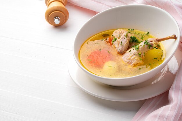 Chicken soup with vegetables in white bowl on wooden table