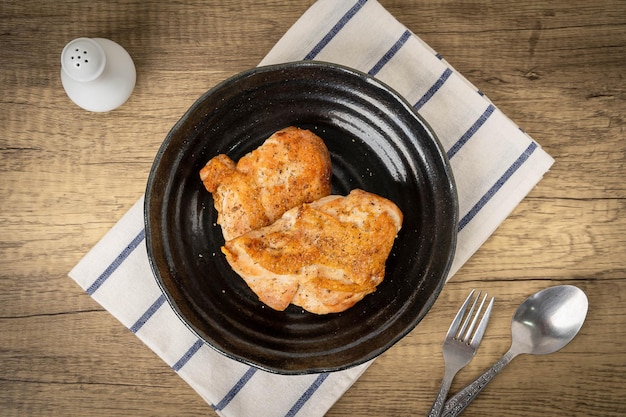 木製のテーブルの上にある黒い皿のチキンステーキ体に必要なタンパク質に満ちた食べ物