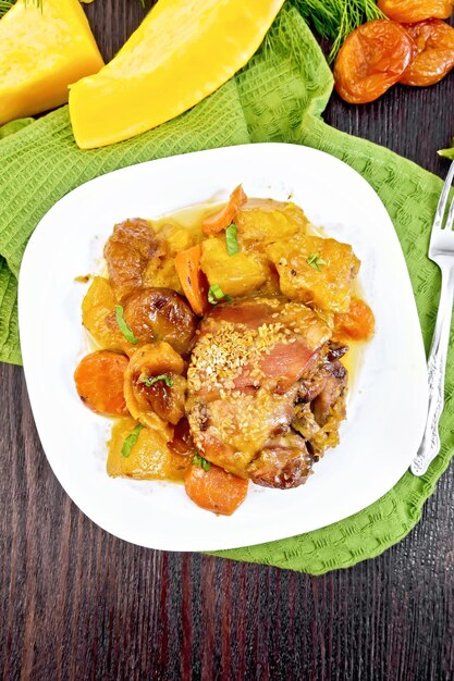 Chicken stew with pumpkin dried apricots carrots and red wine sprinkled with sesame seeds in a plate on towel against the background of dark wooden boards on above