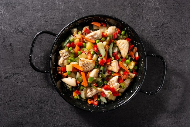 Pollo saltato in padella e verdure su sfondo di pietra nera