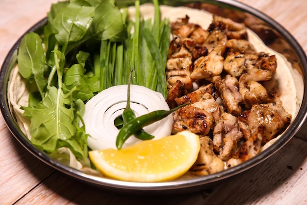 Куриный тикка Даджадж с дольками салата, лимоном и соусом, подаваемый в блюде, изолированном на фоне арабской кухни
