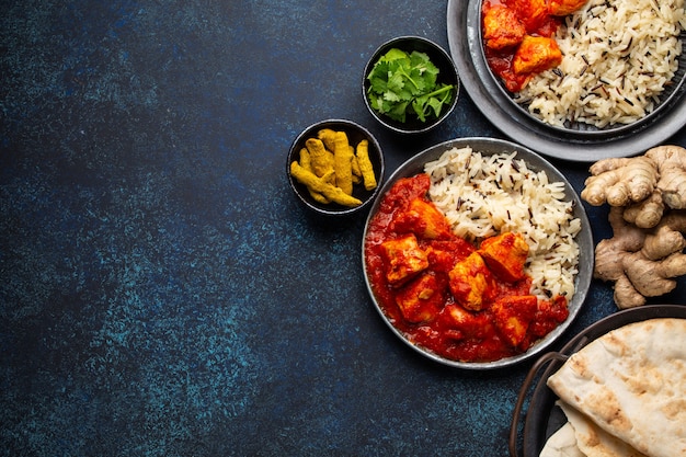 Chicken tikka masala dish with rice, flat Indian bread and spices in rustic metal plates on concrete background top view. Chicken tomato curry, traditional Indian meal, free space for text