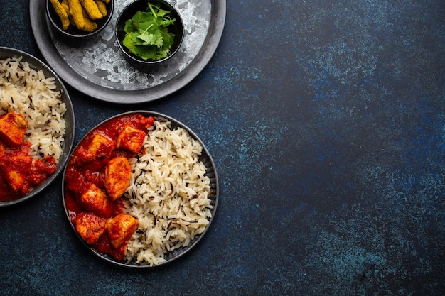 Chicken tikka masala dish with rice, flat Indian bread and spices in rustic metal plates on concrete background top view. Chicken tomato curry, traditional Indian meal, free space for text