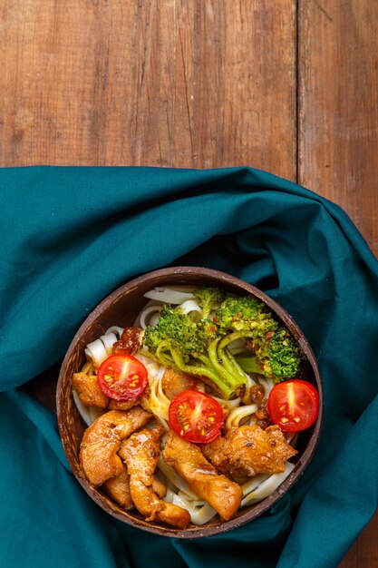 Chicken udon in Japanese sauce on a plate of coconut shells on a blue napkin Vertical photo