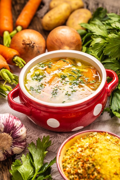 Chicken or vegetable soup broth in a vintage bowl with homemade noodles carrot onion celery herbs garlic and fresh vegetables.