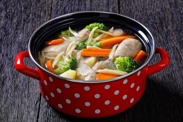 Chicken vegetable soup with pasta in red pot