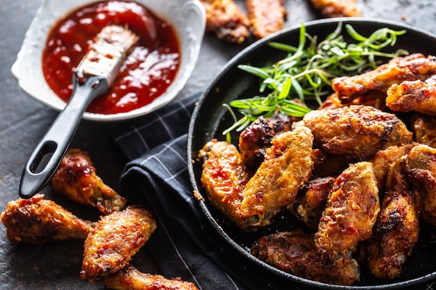 Chicken wings barbeque in a cast iron baking dish with BBQ sauce and rosemary.