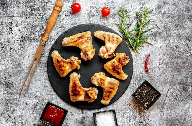 Chicken wings on a black plate with spices and herbs on a gray background.