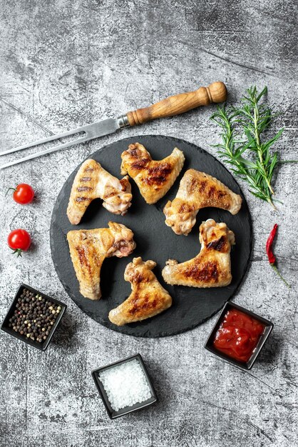 Chicken wings on a black plate with spices and herbs on a gray background.