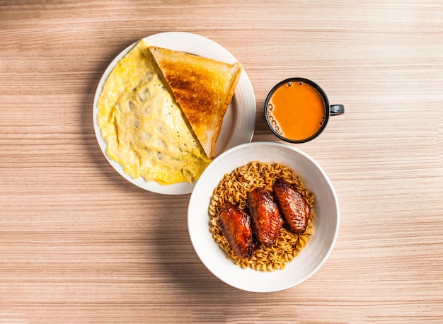 Фото Куриные крылья, лапша с омлетом, хлеб, тост и кофе, подаваемые в блюде, изолированном на столе. вид на завтрак в гонконге.