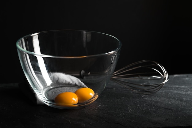 Chicken yolks in a bowl and whisk for beating on a gray table horizontal