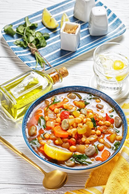 Chickpea and green broad bean Moroccan soup in a blue bowl on a white wooden table, vertical view