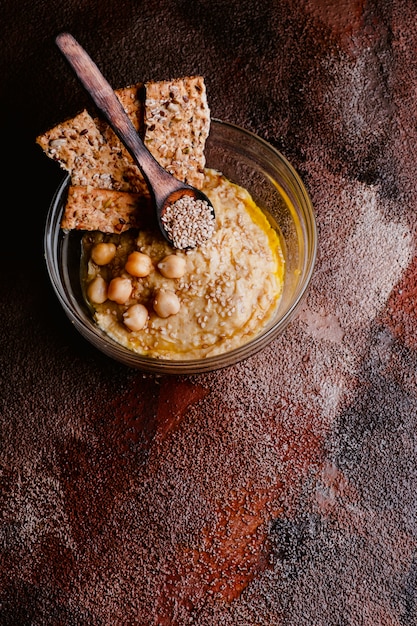 Chickpea hummus with sesame in glass bowl on wooden table. Vegan food