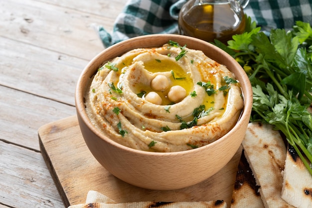 Chickpea hummus in a wooden bowl garnished with parsley paprika and olive oil isolated on white background