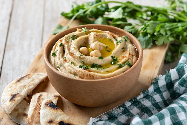 Chickpea hummus in a wooden bowl garnished with parsley paprika and olive oil on wooden table