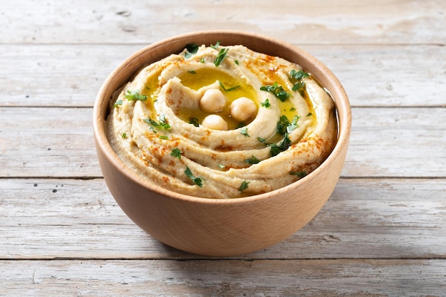 Chickpea hummus in a wooden bowl garnished with parsley paprika and olive oil on wooden table