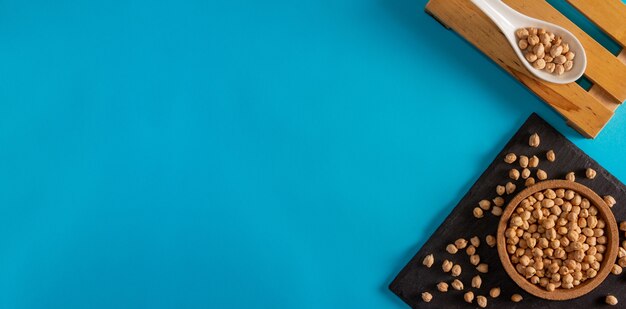 Chickpeas in cork bowl and slate surface with porcelain spoon on blue background Copy space