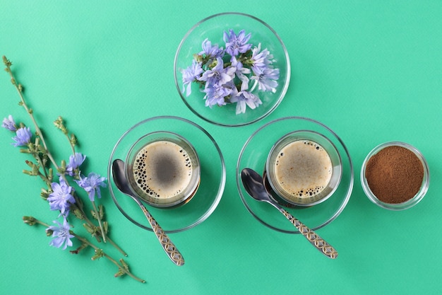 Chicory beverage in two glass cups, with concentrate and flowers on green