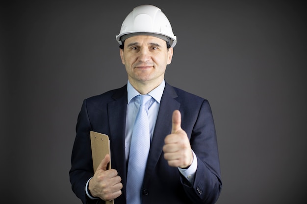 Chief engineer in hard hat with clipboard showing like sign with thumb up