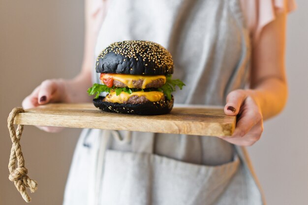 The chief is holding a wooden cutting Board with a black Burger.