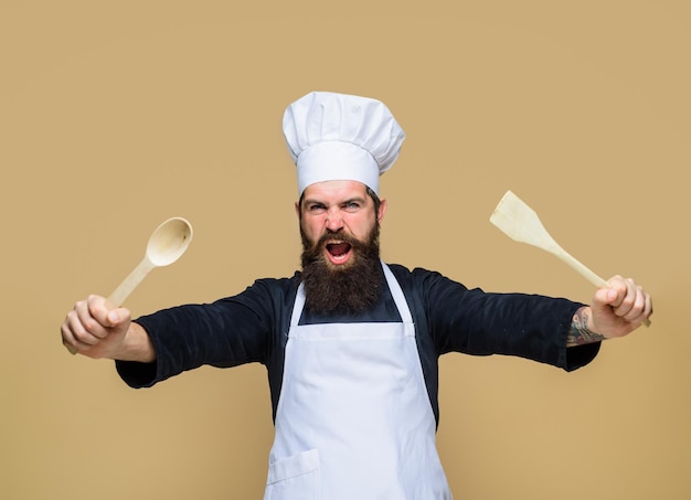 Chief man in kok uniform houdt houten keuken kookgerei bebaarde man bereidt zich voor om voedsel te koken