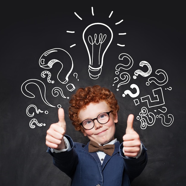 Child 9 years old having fun and showing thumb up on blackboard background with lightbulb