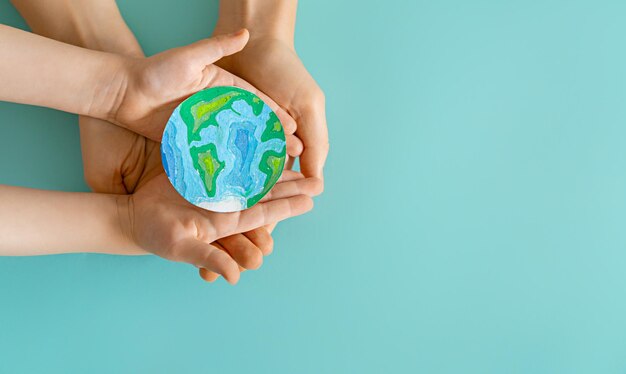 Child and adult holding planet in hands on teal background. Earth day holiday concept.