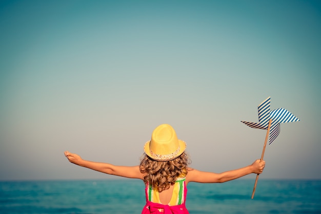 Foto bambino contro il mare blu e il cielo che tiene una girandola durante le vacanze estive