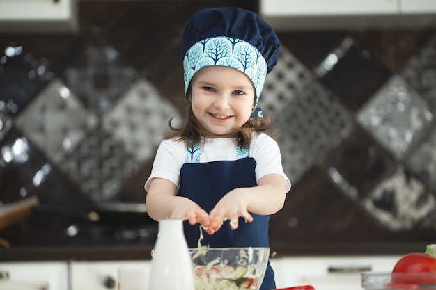 Child in an apron and a chef's hat is stirring a vegetable salad in the kitchen